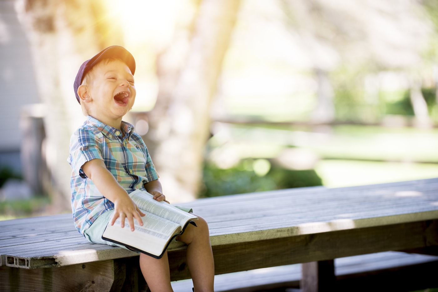 A young boy laughing joyfully while sitting outdoors with a book