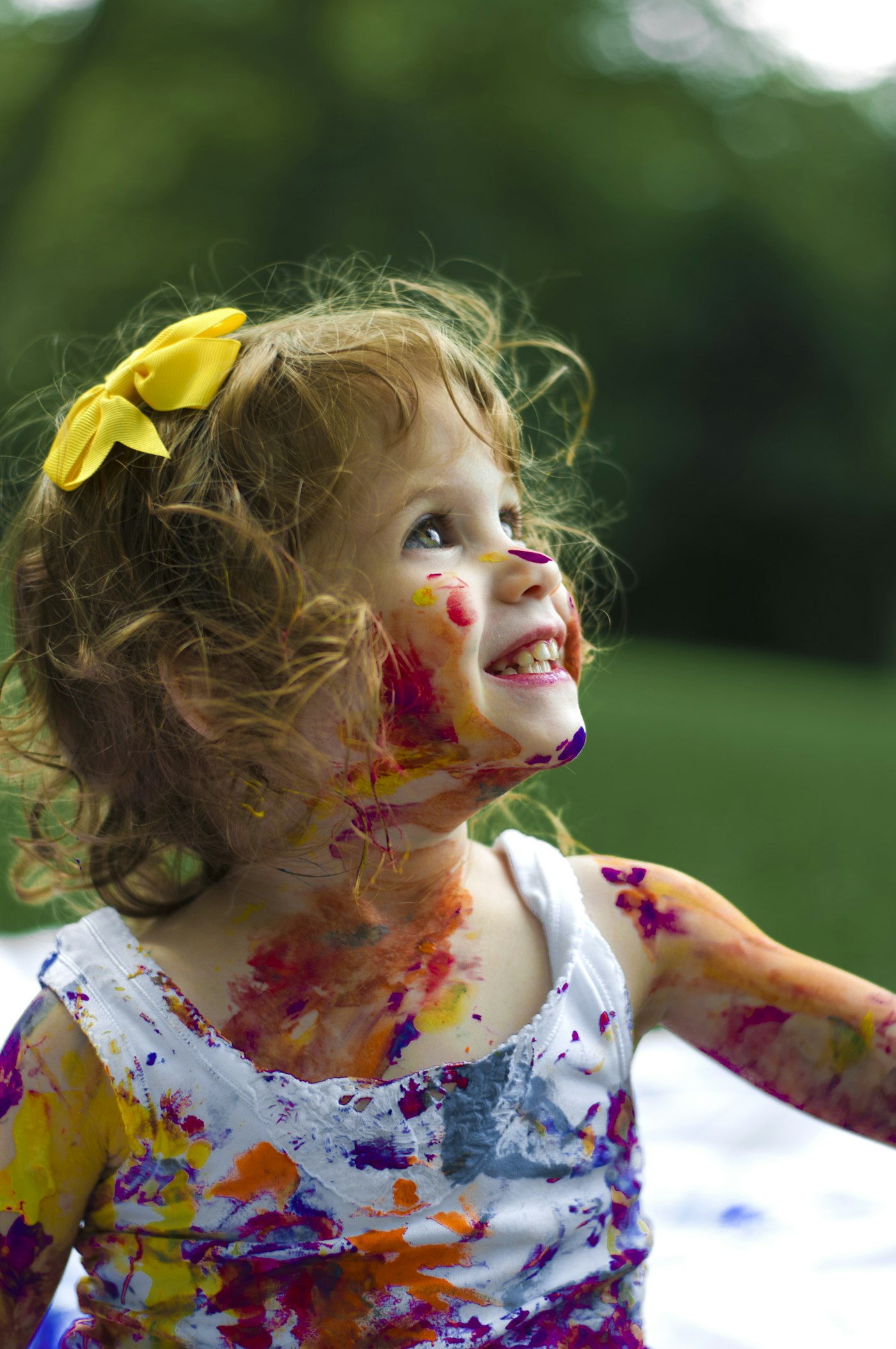 A joyful little girl with a yellow bow laughing during a messy paint activity