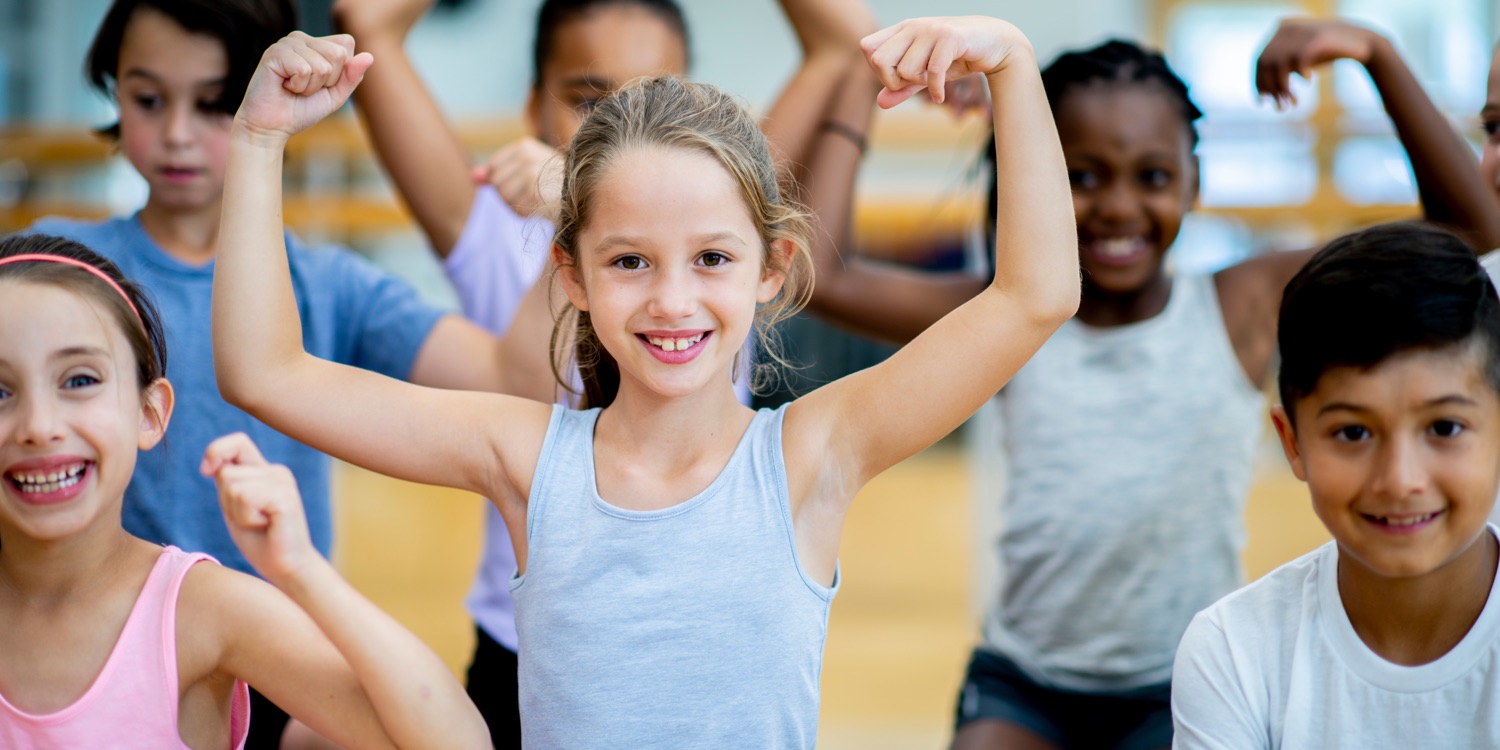 A group of smiling children flexing their arms during a fitness class