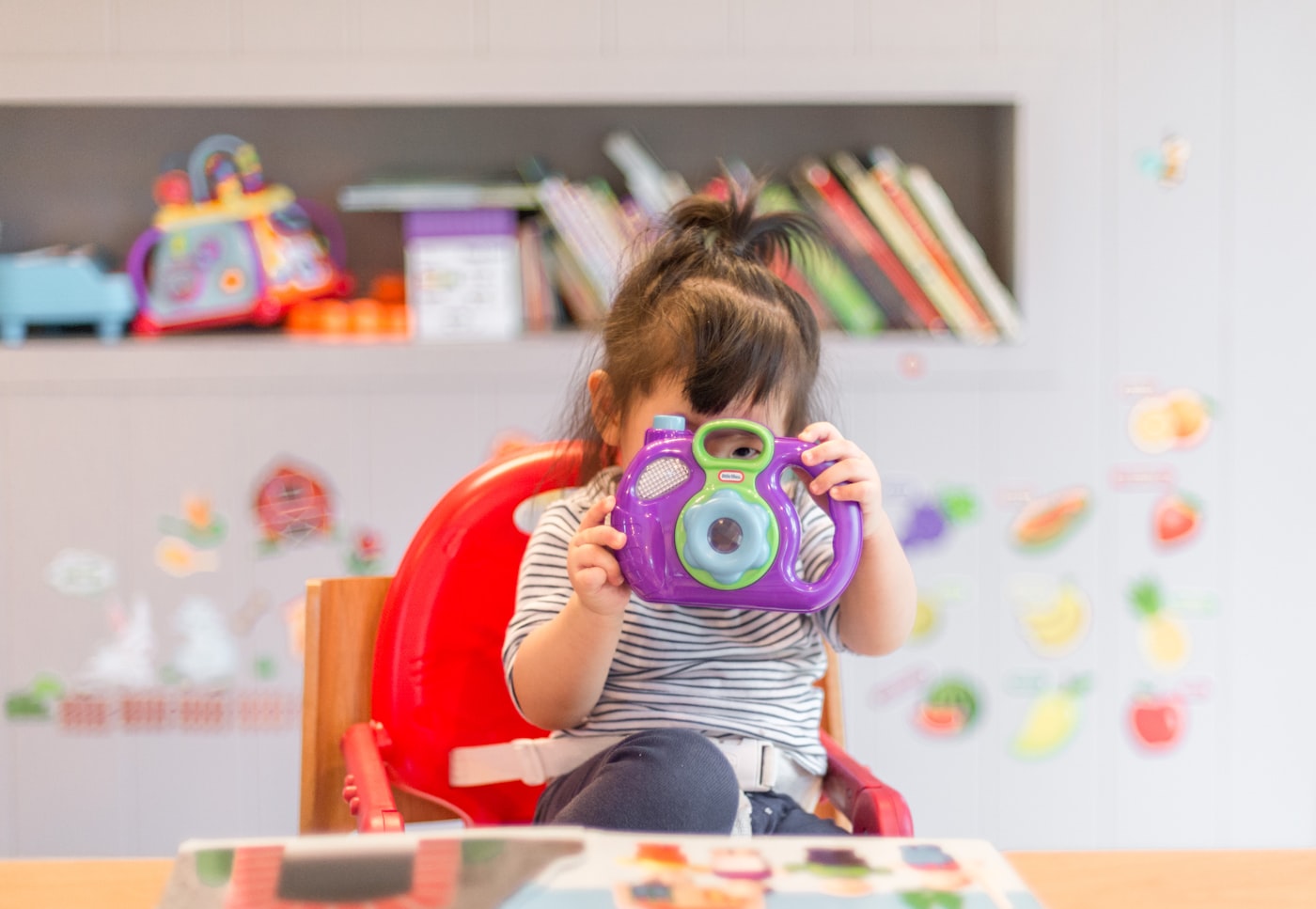 A toddler exploring a colorful toy camera in a bright playroom